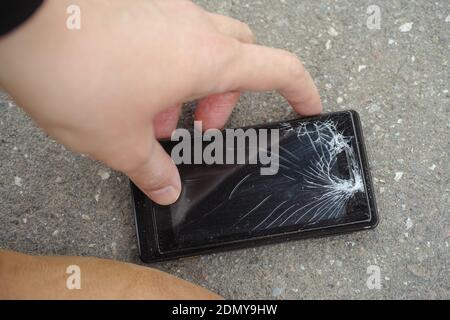 Eine Person, die ein gefallenes Smartphone aufgreift. Smartphone mit gesprungenem Bildschirm. Nahaufnahme. Stockfoto