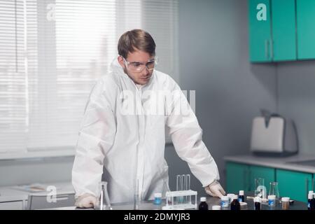 Junge nachdenkliche Chemikerin, die sich in einem hellen Labor auf den Tisch lehnt. Stockfoto
