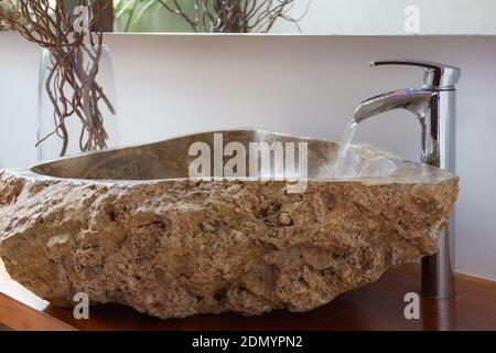 Wasser läuft aus Bad Wasserhahn in original Stein Waschbecken mit Dekoration Äste auf Glasvase auf der Seite. Luxuriöses Interior Design Konzept Stockfoto