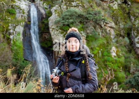 Junge, schöne weiße kaukasische Frau in einem lächelnden Winterhut mit einem Wasserfall Stockfoto