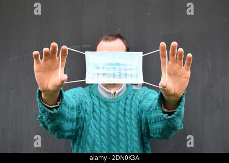 Maske von Menschenhänden gehalten mit grünem Pullover auf dunkelgrauem Hintergrund. Stockfoto