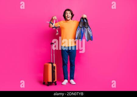 In voller Länge Foto von Kerl Gepäck zeigen Maske klappt auf Mund tragen orange T-Shirt Jeans Sneakers isoliert rosa Farbe Hintergrund Stockfoto