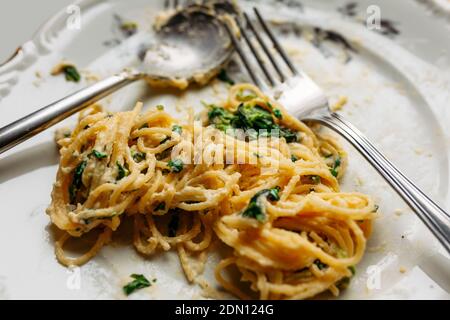 Spaghetti in cremiger Spinat-Sauce mit Käse, auf einem unordentlichen Blumenplatte mit silberner Gabel und Löffel, halb gegessen, Nahaufnahme Stockfoto