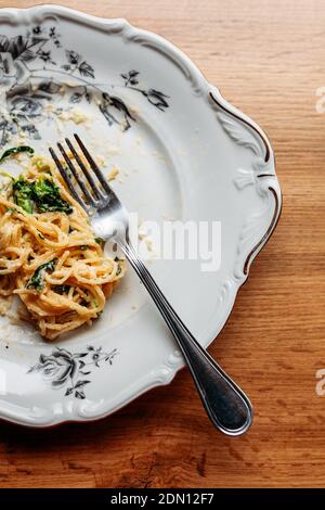 Spaghetti in cremiger Spinat-Sauce mit Käse, auf einem unordentlichen Blumenplatte mit silberner Gabel, halb auf einem Tisch gegessen Stockfoto