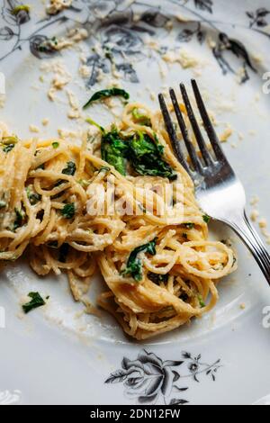 Spaghetti in cremiger Spinat-Sauce mit Käse, auf einem unordentlichen Blumenplatte mit silberner Gabel, halb gegessen Stockfoto