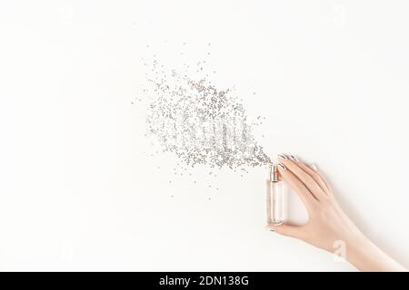 Weibliche Hand mit trendigen silbernen Nagel-Design hält stilvolle Flasche Parfüm mit Spray von silbernen Stern geformt funkelt auf weißem Hintergrund. Luxus pro Stockfoto
