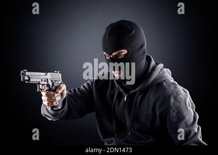 Criminal trägt schwarze Balaclava und Kapuzenpullover mit einer Waffe in Die Dunkelheit Stockfoto