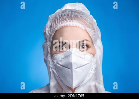 Nahaufnahme Porträt einer Ärztin mit Schutzanzug gegen die Coronavirus-Pandemie covid-2019. Müder Arzt auf blauem Hintergrund Stockfoto