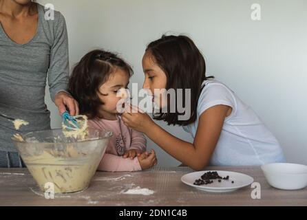 Mutter und ihre beiden Töchter bereiten in ihrer Küche Kekse mit Schokolade zu. Stockfoto