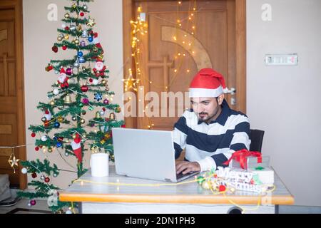 Junger indischer Mann mit Laptop-Computer während der weihnachtsferien, Arbeit von zu Hause während Pandemie, Winter, dezember, neue normale. Stockfoto