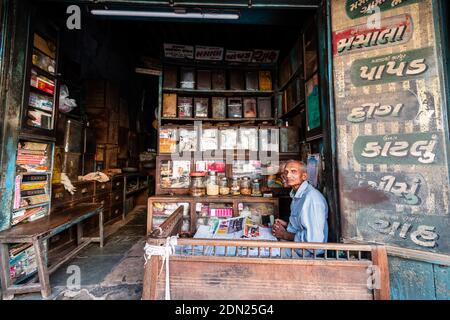 Jamnagar, Gujarat, Indien - Dezember 2018: Ein indischer Ladenbesitzer sitzt in seinem Lebensmittelgeschäft und verkauft Gewürze und Snacks. Stockfoto