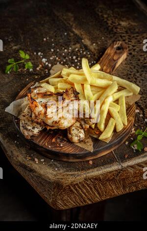Grillhaus Konzept. Gegrilltes, gebratenes, gebratenes, leckeres Hühnerfleisch mit pommes auf dem alten Holzschneidebrett. Stockfoto