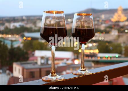 Zwei Weingläser auf dem Balkon mit verschwommener Abendstadt Im Hintergrund anzeigen Stockfoto