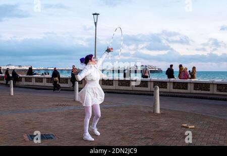 Brighton UK 17. Dezember 2020 - AA Hula Hooping Busker unterhält Besucher an der Küste von Brighton am Ende eines hellen Tages an der Südküste . Die Stadt Brighton und Hove wurde in Coronavirus Tier zwei Beschränkungen in England nach einer Ankündigung heute von der Gesundheitsminister Matt Hancock gehalten : Credit Simon Dack / Alamy Live News Stockfoto