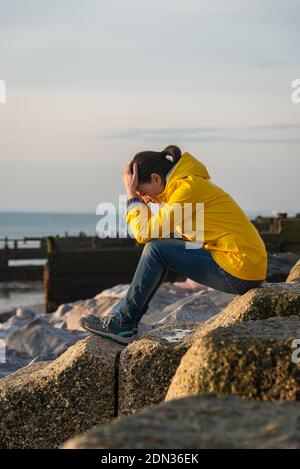 Frau sitzt auf Felsen mit dem Kopf in den Händen. Stockfoto