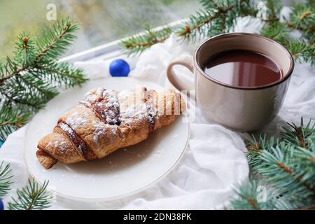 Dampfende Tasse heißen Kaffee mit Croissant stehen auf dem Fenster in Snowy Winter Tag. Konzept Für Den Weihnachtsmorgen Stockfoto