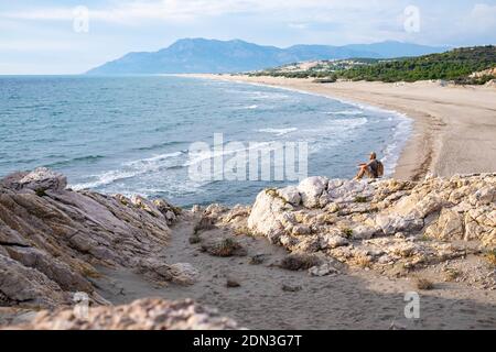 Patara Strand, Südtürkei. Mann, der auf einem Felsen sitzt. Stockfoto