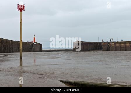 Blick von der Bootsrampe über Watchet Harbour, Somerset, England, Großbritannien bei Ebbe, mit Blick auf die Wellenbrecher und den Leuchtturm. Stockfoto