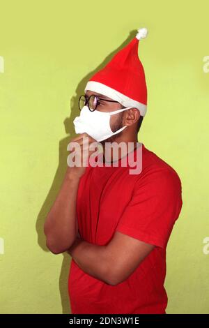 Weihnachten während der Pandemie des COVID-19 Coronavirus. Mann trägt chirurgische Gesichtsmaske und Santa Hut. Männliches Model Denken im weihnachtsmann Kostüm. Stockfoto