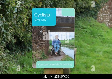 A sign by a bridge telling cyclists to give way to pedestrians and other towpath users on the Grand Western Canal at Sampford Peverell in Devon. Stock Photo