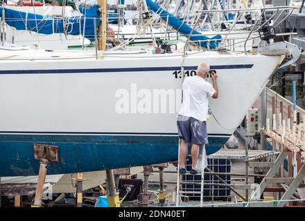 Mann, der Registrationsnummern auf der Yacht im Bootshof einlegt. Stockfoto
