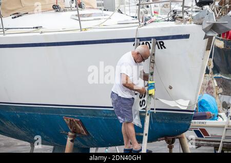 Mann, der Registrationsnummern auf der Yacht im Bootshof einlegt. Stockfoto
