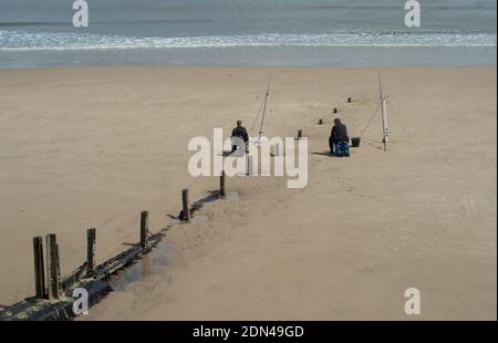 Zwei Angler Angeln vom Strand sitzen auf beiden Seiten Eine alte Stumper und in der Tat sozial distanziert Stockfoto