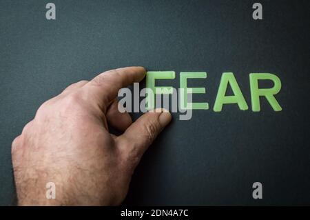 Menschliche Finger entfernt das Wort Angst geschrieben mit Plastikbuchstaben auf dunkelgrauem Papierhintergrund, Konzept Stockfoto