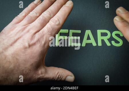 Menschliche Hand verbirgt das Wort Angst geschrieben mit Plastikbuchstaben auf dunkelgrauem Papierhintergrund, Konzept Stockfoto
