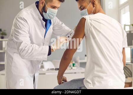 Young doctor in face mask giving coronavirus or flu antiviral vaccine to patient Stockfoto