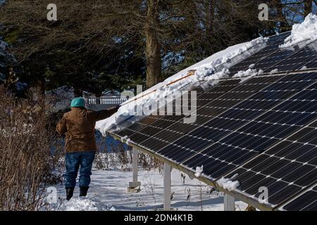 Frau, die schneebedeckte Sonnenkollektoren an einem hellen und kalten Wintertag reinigt. Stockfoto