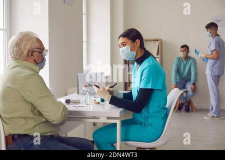 Asiatische Ärztin interviewt einen älteren Mann, der zur Impfung ins Krankenhaus kam. Stockfoto