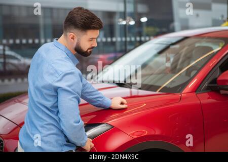 Rückansicht eines männlichen Kunden, der bei einem Autohändler ein rotes Auto untersucht, Kopierraum Stockfoto