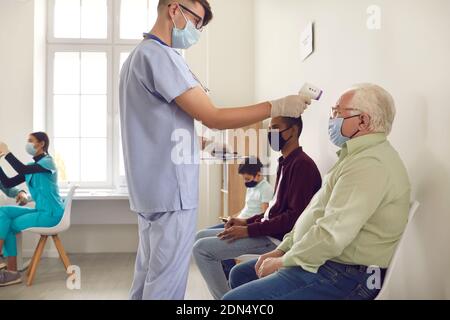 Medizinisches Personal, das die Temperatur eines älteren Mannes mit einem berührungslosen elektronischen Thermometer misst Stockfoto