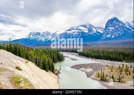 Bewaldete Tal und Fluss in der Nähe von Bergen unter niedrigen Wolken, am Athabasca River, Alberta, Kanada. Stockfoto