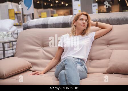 Charming mature woman sitting on a couch, looking away, shopping for new furniture Stockfoto