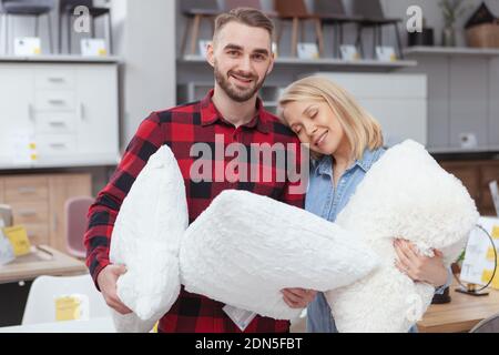 Fröhliches junges Couple, das neue Kissen im Einrichtungsgeschäft kauft. Charmanter junger Mann und Frau, die gerne für ihre neue Wohnung einkaufen Stockfoto