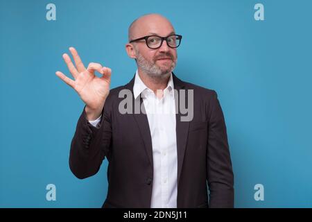 Reife gut aussehende Mann mit Bart zeigt ok Zeichen mit Fingern. Studio auf gelber Wand. Stockfoto