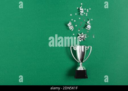 Winner or champion silver trophy cup with confetti on green background top view. Winning or success concept. Stock Photo