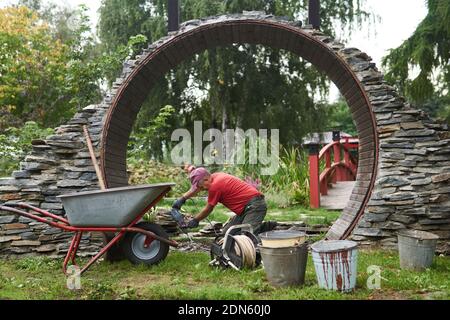 Perm, Russland - 01. September 2020: Arbeiter baut einen runden Eingang namens Mondtor in einem chinesischen Garten Stockfoto