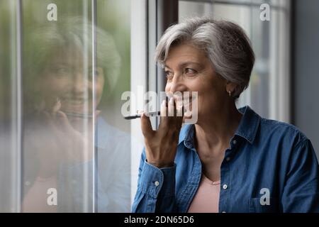 Glückliche ältere Frau im mittleren Alter, die eine Audiobotschaft aufzeichnet. Stockfoto