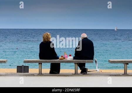 Rückansicht eines Paares auf einer Bank in der Nähe des Meeres Essen und Trinken. Stockfoto