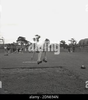 1960er, historisch, Vorderansicht eines jungen Mannes, draußen auf einem Sportplatz, der den langen Sprung macht, gestreckte Beine in eine Sandgrube bei einem County Sporttag, Fife, Schottland, Großbritannien. Stockfoto