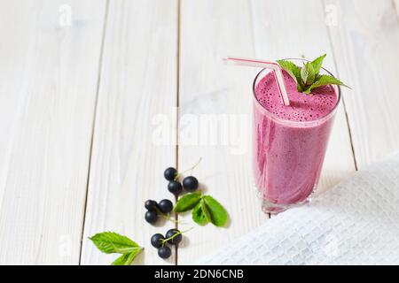 Vitamin Cocktail aus schwarzen Johannisbeeren, Eis, Milch in einer Glastasse. Kunststoffrohr und Minze. Holz weiß Hintergrund und Geschirrtuch. Horizontales Bild Stockfoto