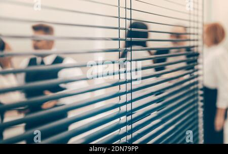 Durch die Jalousien. Mitarbeiter des Unternehmens am Arbeitsplatz im Büro. Stockfoto