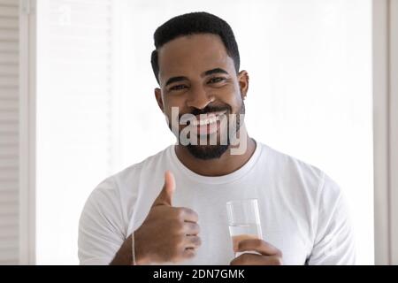 Junger afrikanischer Mann mit Daumensup-Geste, mit einem Glas Wasser. Stockfoto