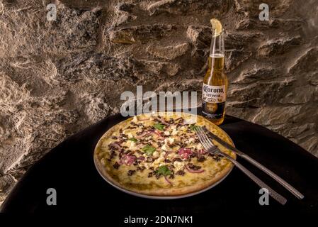 Arinsal, Andorra: 2020. Dezember 16: Mexikanische Pizza mit frischem Käse, Zwiebeln und Koriander, begleitet von einem Corona Bier im Winter 2020. Stockfoto