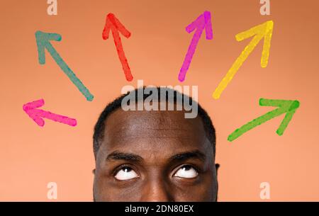 Confused black Man has to choose the right arrow to follow. Concept of options, confusion, decision. Stock Photo