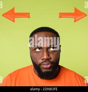 Confused black Man has to choose the right arrow to follow. Concept of options, confusion, decision. Stock Photo