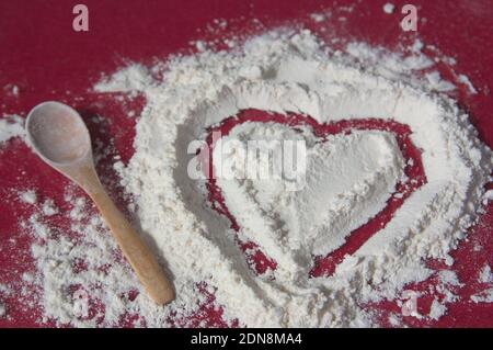 Kneading table in which a heart has been drawn on a pile of flour next to a wooden spoon Stockfoto